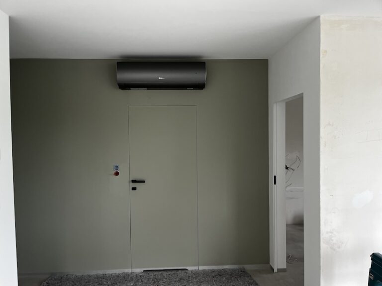 Jednostka wewnętrzna klimatyzacji, wisząca na oliwkowej ścianie.